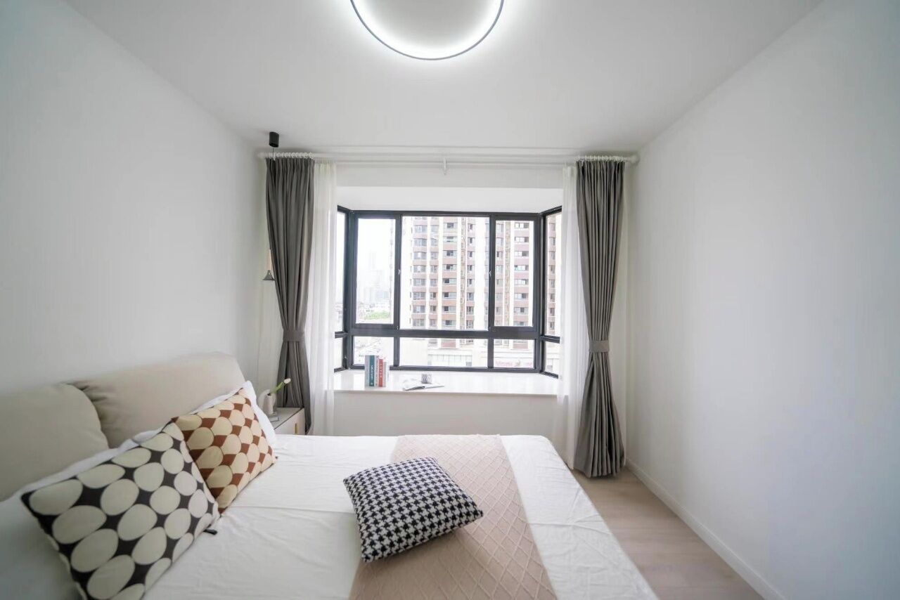 A bedroom with a large bed, a window with curtains, and a view of buildings outside.