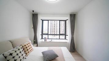 A bedroom with a large bed, a window with curtains, and a view of buildings outside.