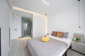 Un dormitorio moderno con una cama, un espejo grande, una mesita de noche y una lámpara de pared.