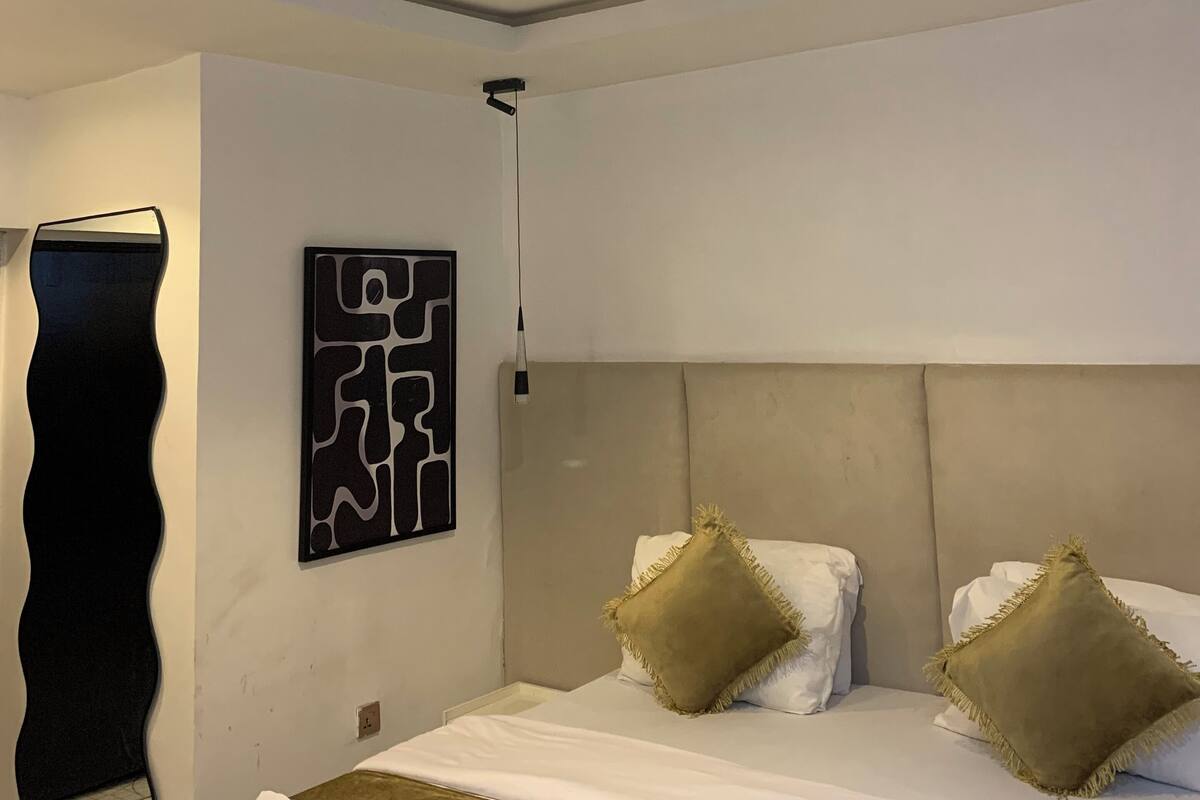 Ein modernes Hotelzimmer mit einem großen Bett, einem Kopfteil, einem Wandbild und einer Deckenleuchte.