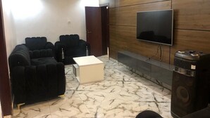 Un salon moderne avec un grand téléviseur à écran plat fixé à un mur en bois, un canapé d’angle noir, une table basse blanche et un sol à motifs de marbre.