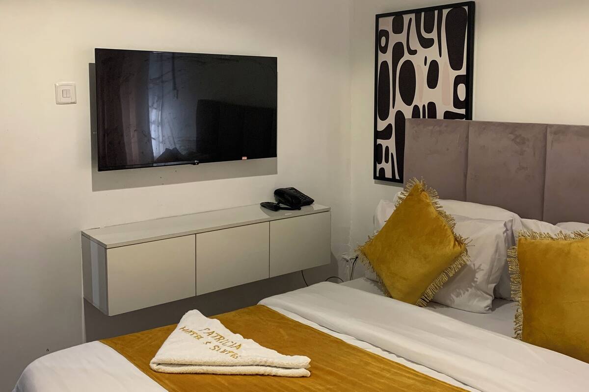 Ein modernes Hotelzimmer mit einem Bett, einem flachbildfernseher an der Wand, einem Nachttisch mit Telefon und einem dekorativen Wandbild.