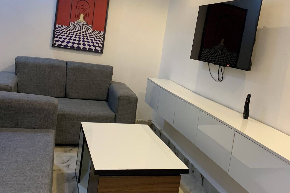 Ein modernes Wohnzimmer mit einem grauen Sofa, einem Holztisch, einer weißen TV-Konsole und einer Wandklimaanlage.