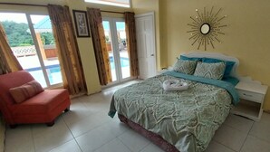 Une chambre à coucher avec un lit, une table de chevet, un fauteuil rouge et une vue sur une piscine, visible à travers une porte vitrée.