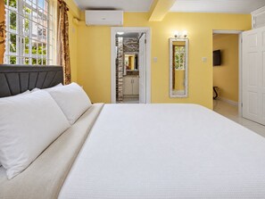A bedroom with a bed, a window with curtains, an air conditioning unit, and a door leading to a bathroom. - Union Hilltop Paradise Villas (Castries)