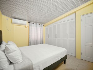 A bedroom with a bed, an air conditioning unit, a set of white louvered closets, and a door. - Union Hilltop Paradise Villas (Castries)
