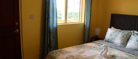 A bedroom with a bed, curtains, a nightstand, and a window.