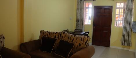 A living room with a brown sofa, a dining table, and a door.