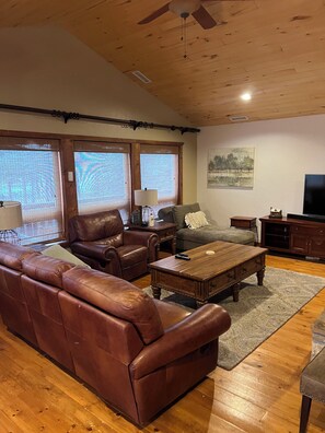 Ein Wohnzimmer mit einem braunen Ledersofa, einem Holztisch und einem Fernseher auf einer Holzkommode.