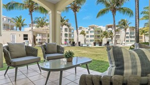 Une terrasse d’hôtel avec deux fauteuils rembourrés, une table à plateau en verre et une vue sur une piscine et des palmiers.