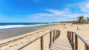 Une promenade en bois qui mène à une plage, avec un ciel dégagé et des vagues calmes.