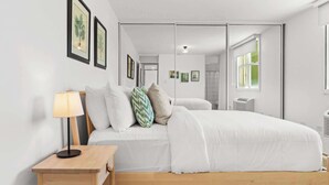 Une chambre moderne avec un lit, une table de chevet, une lampe et des reproductions encadrées de motifs botaniques accrochées au mur.