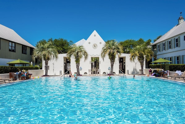 A swimming pool with palm trees, a building with a clock, and a clear blue sky.