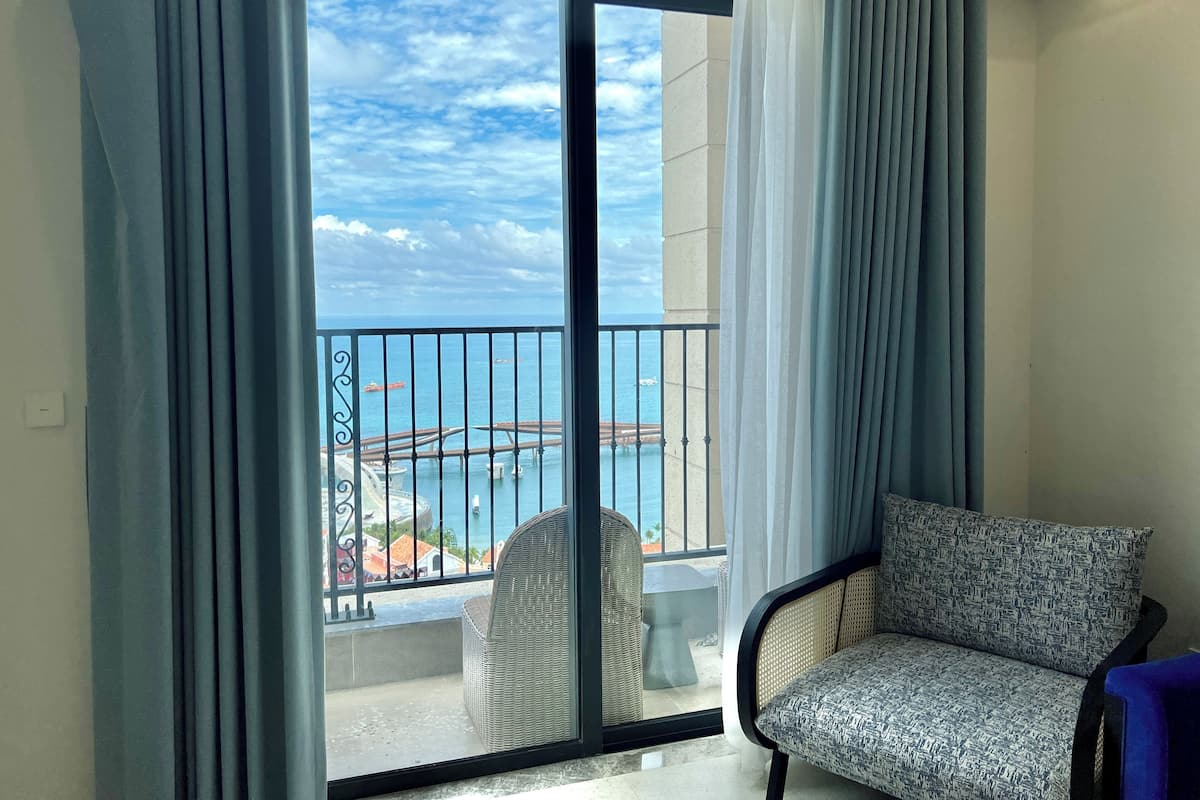 A balcony with a view of the sea and a bridge, a wicker chair, and a sofa.