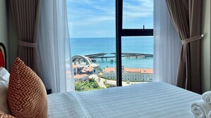 Een hotelkamer met een groot raam met uitzicht op zee en een brug.