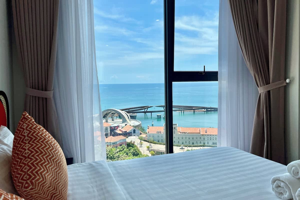 A hotel room with a large window offering a view of the sea and a bridge.