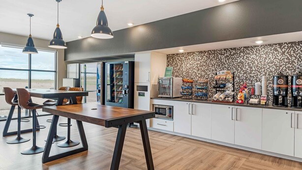 A modern kitchen with a wooden table and bar stools, a coffee station, and a view of the beach. - Extended Stay America Premier Suites - Yuma (Yuma)