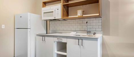 A compact kitchen with white cabinetry, a built-in microwave, and a sink.