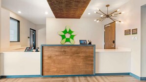 A reception area with a wooden reception desk, a green abstract wall decoration, a modern chandelier, and a wooden ceiling. - Extended Stay America Premier Suites - Yuma (Yuma)