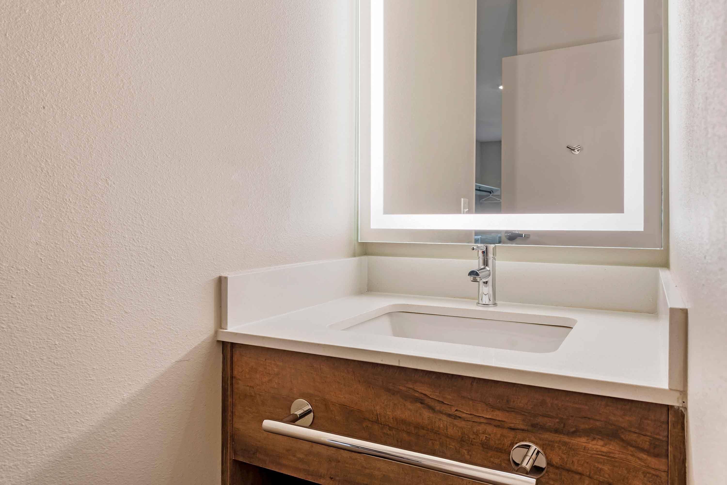 A bathroom with a white sink, a mirror, and a wooden vanity with a drawer.
