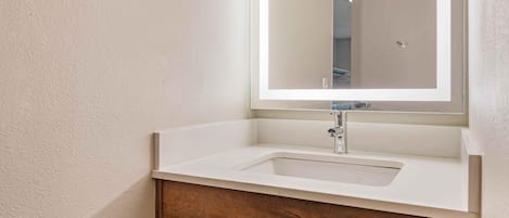 A bathroom with a white sink, a mirror, and a wooden vanity with a drawer.