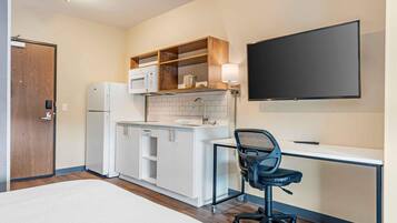 Habitación de hotel compacta con kitchenette, una cama, un escritorio con silla y televisión montada en la pared.