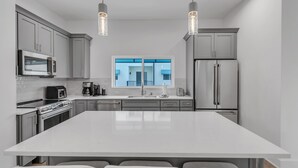 Una cocina moderna con una isla grande, electrodomésticos de acero inoxidable e iluminación colgante.