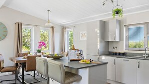 Una cocina moderna con una isla central, taburetes de bar, una mesa de comedor y vistas al exterior.