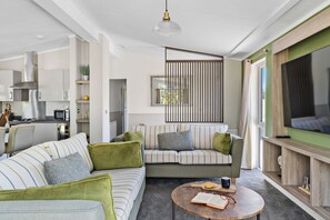 Relax in this stylish living space with a large sofa, TV unit, and kitchen area.