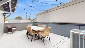 Eine Dachterrasse mit Tisch und Stühlen, Lichterketten und einer Klimaanlage.