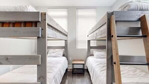 Ein Schlafsaalzimmer mit Etagenbetten, einem kleinen Tisch und einem Fenster mit Jalousien.