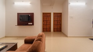 A spacious living area with a sofa, a flat-screen TV mounted on the wall, and a pair of wooden doors. - Infinity stays (Puducherry)