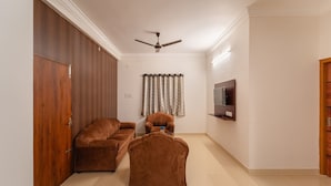 A living room with a sofa set, a chair, a ceiling fan, a television, and a wardrobe. - Infinity stays (Puducherry)