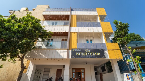 A multi-story building with a sign for 'Infinity Stays' indicating luxury accommodation. There are motorcycles parked in front, and the building has a modern architectural style with balconies. - Infinity stays (Puducherry)