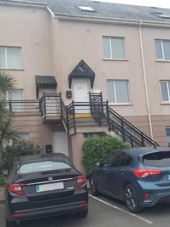 A building with a beige facade, a black staircase, and a white door. There are two cars parked in front. - Sea front Apartment in Tramore (Tramore)