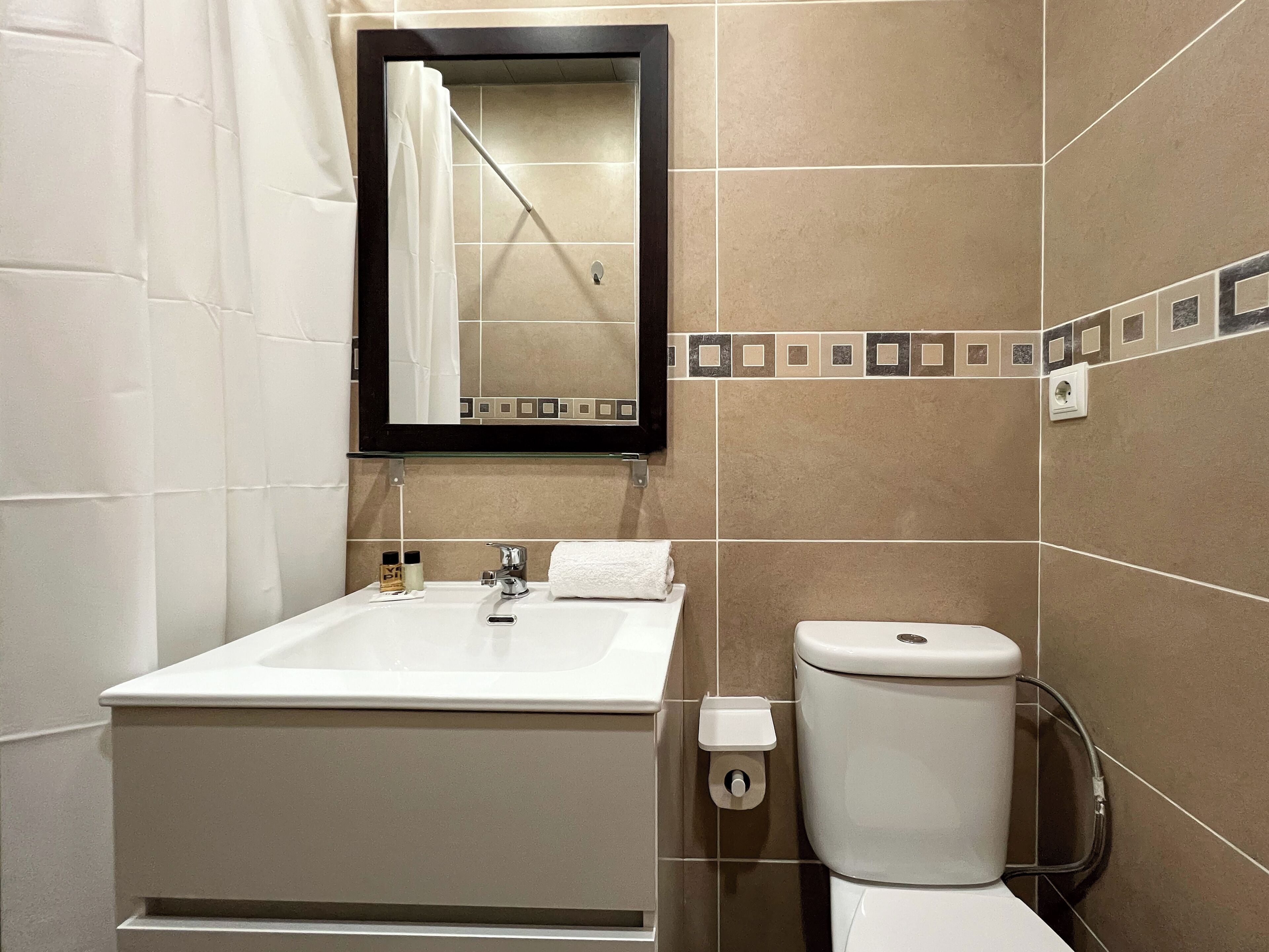 A bathroom with a white sink, a mirror, a toilet, and a shower curtain.