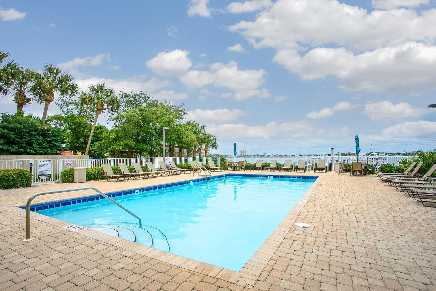 A rectangular pool with a tiled edge, surrounded by lounge chairs and a brick walkway.