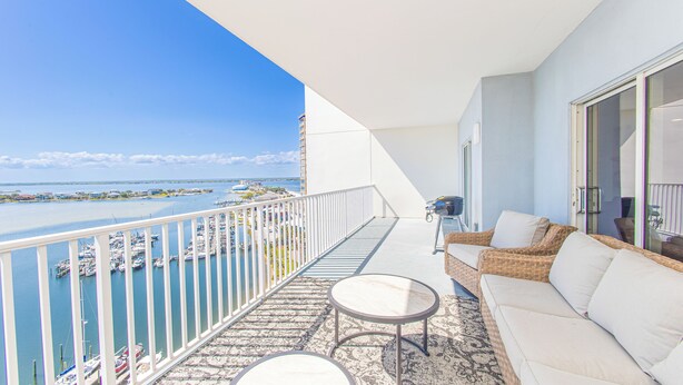 A balcony with a view of a marina, a wicker sofa, and a small round table.