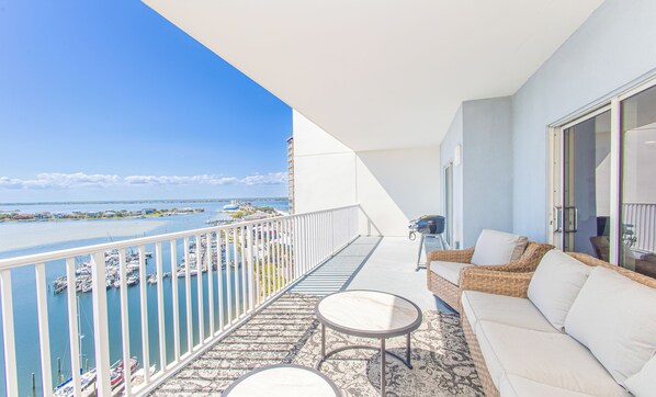 A balcony with a view of a marina, a wicker sofa, and a small round table.