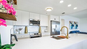 A modern kitchen with white cabinets, stainless steel appliances, and a large island with a gold faucet.