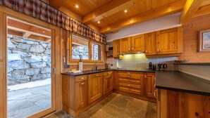 A kitchen with wooden cabinets, a stone backsplash, and a large window with a view of the outside. - Chalet Chafrebelle - sauna & view (Haute-Nendaz)