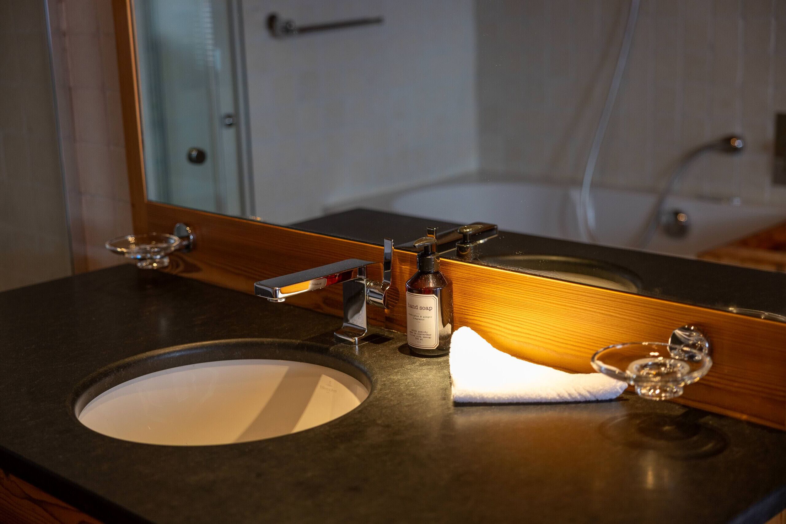 A bathroom with a sink, mirror, and a bottle of hand soap.