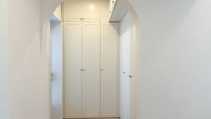 A hallway with a white arched doorway leading to a closet with two doors and a built-in shelf.