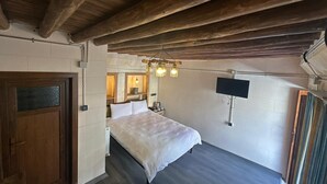 Ett sovrum med ett träpanelat tak, en säng, en tv som är monterad på väggen och ett fönster med gardiner.