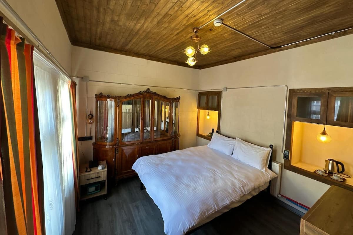 A bedroom with a wooden ceiling, a bed with white bedding, a wooden dresser, and a mirror above the dresser.