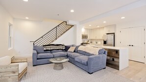 A modern living room with a grey sectional sofa, a round coffee table, and a staircase leading to an upper level.