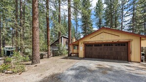 A two-story building with a garage, surrounded by tall pine trees. - 838 Placer Avenue 4 Bedroom Home (South Lake Tahoe)