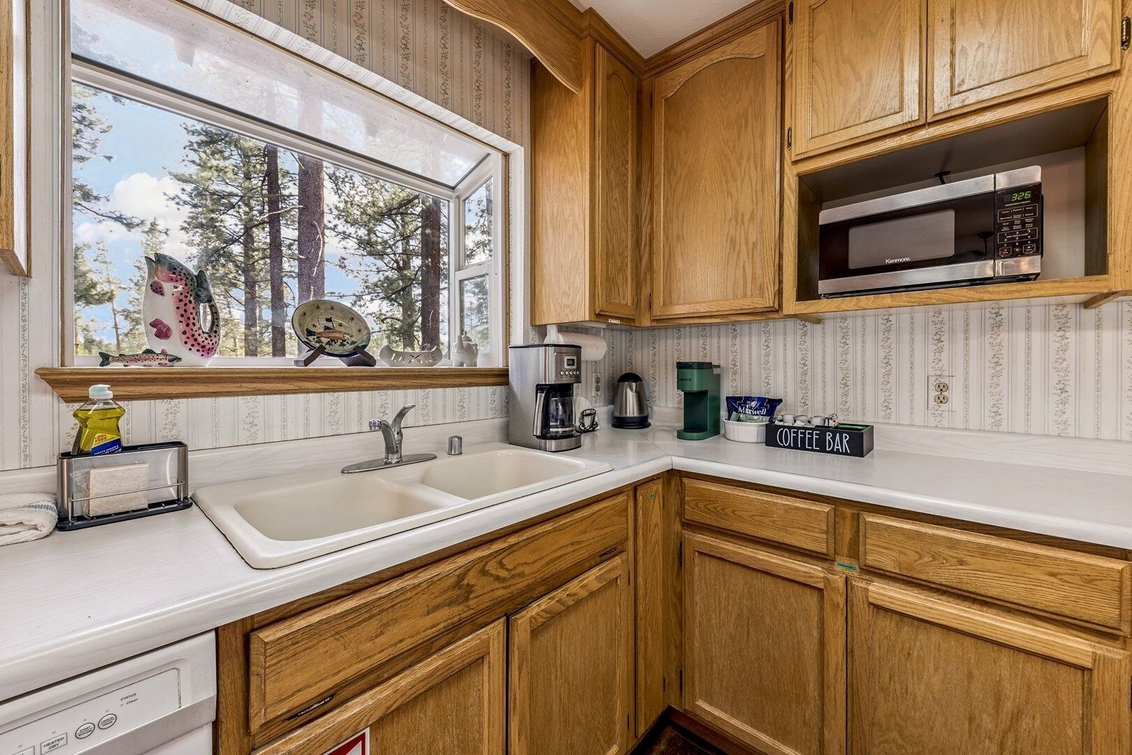 A kitchen with wooden cabinets, a double sink, a microwave, and a coffee station.