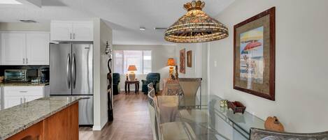 A modern kitchen with a stainless steel refrigerator, a granite countertop, and a dining area with a glass table and chairs.
