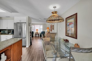 Una cocina moderna con un refrigerador de acero inoxidable, una encimera de granito y una zona de comedor con una mesa y sillas de vidrio.